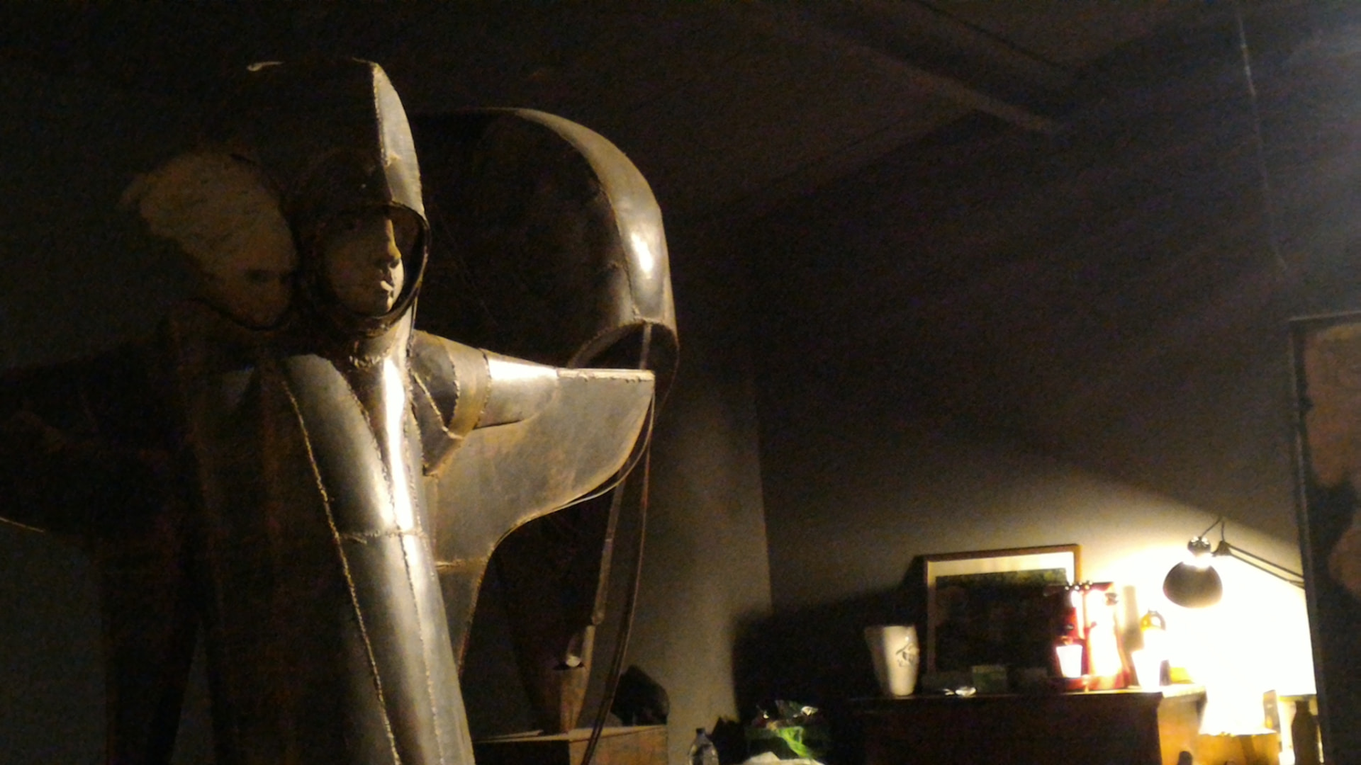 Scultura in lamiera metallica saldata nello studio, con l'atelier illuminato da una lampada sullo sfondo